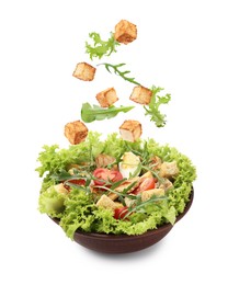 Image of Croutons and other ingredients falling into bowl of salad against white background