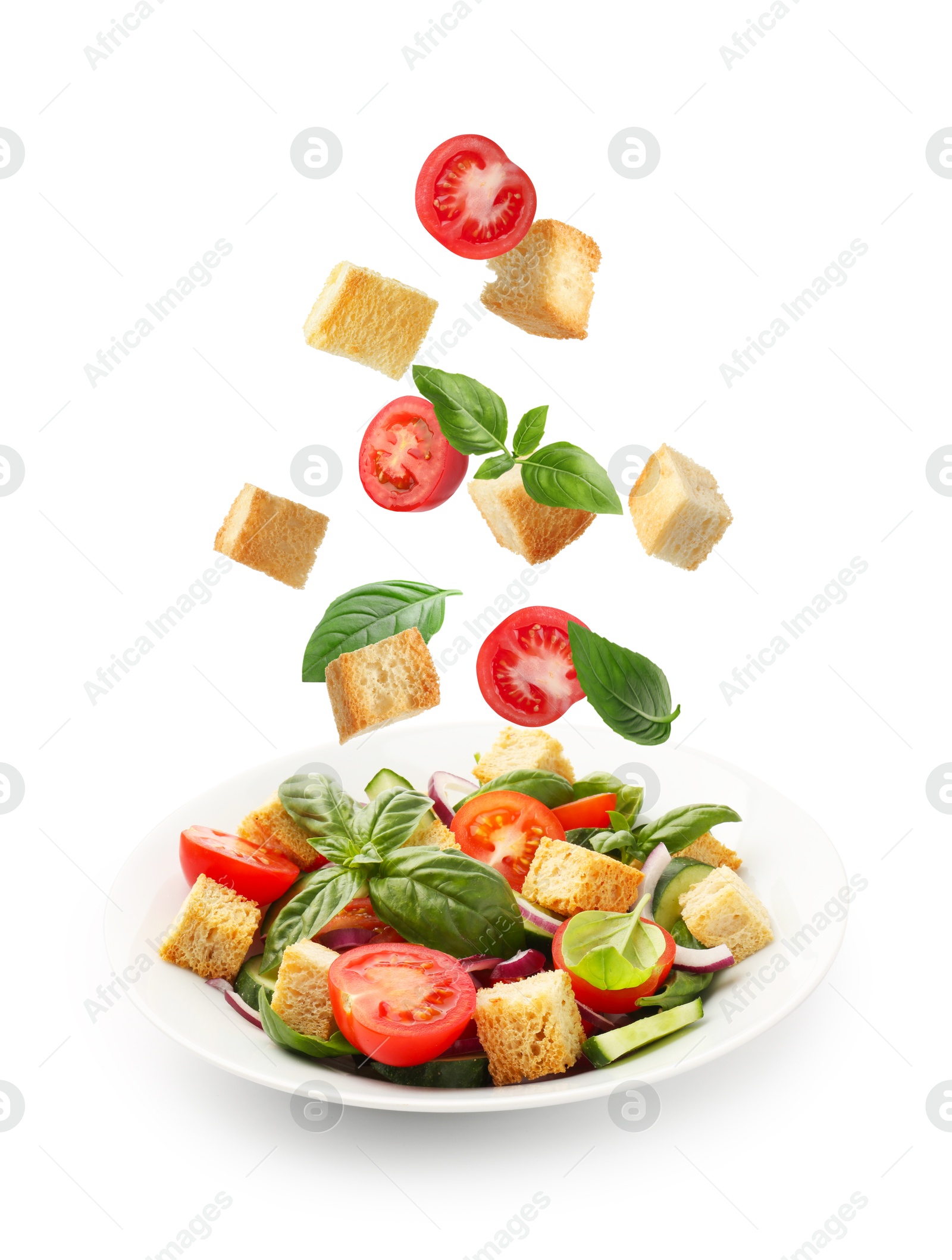 Image of Croutons and other ingredients falling into bowl of salad against white background