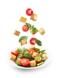 Image of Croutons and other ingredients falling into bowl of salad against white background