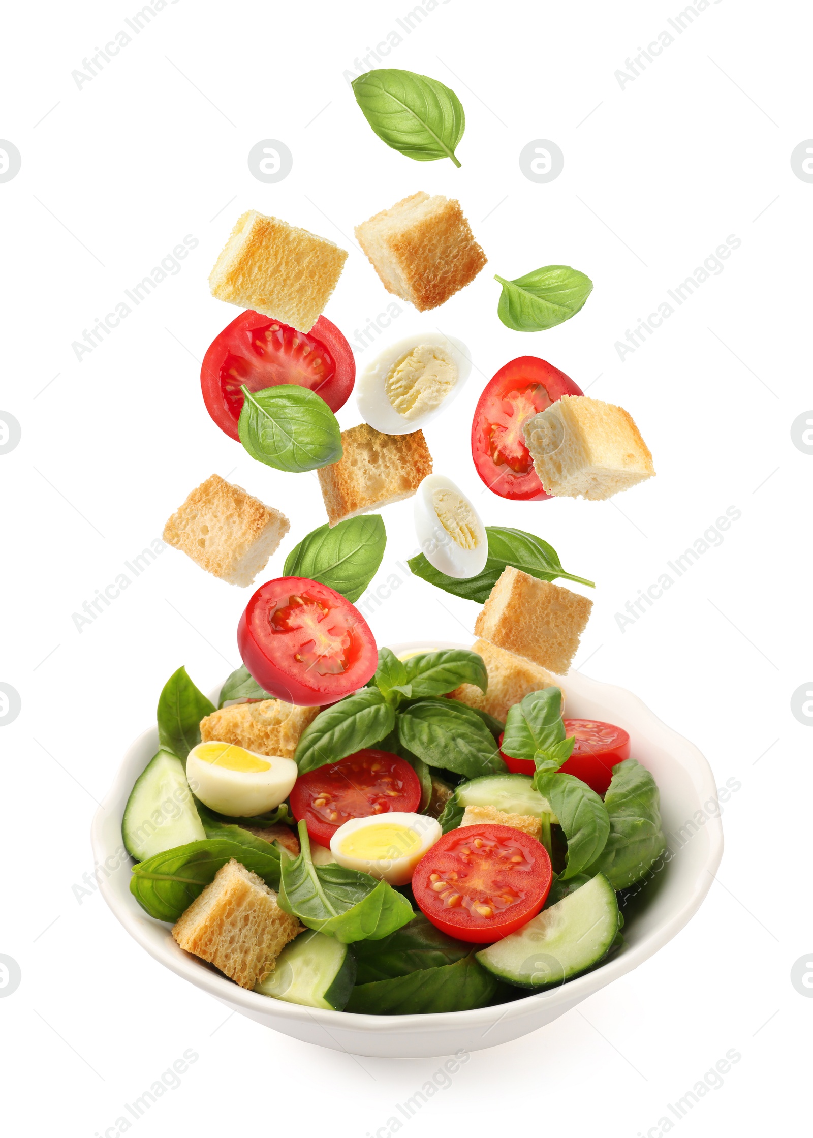 Image of Croutons and other ingredients falling into bowl of salad against white background