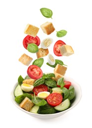 Image of Croutons and other ingredients falling into bowl of salad against white background