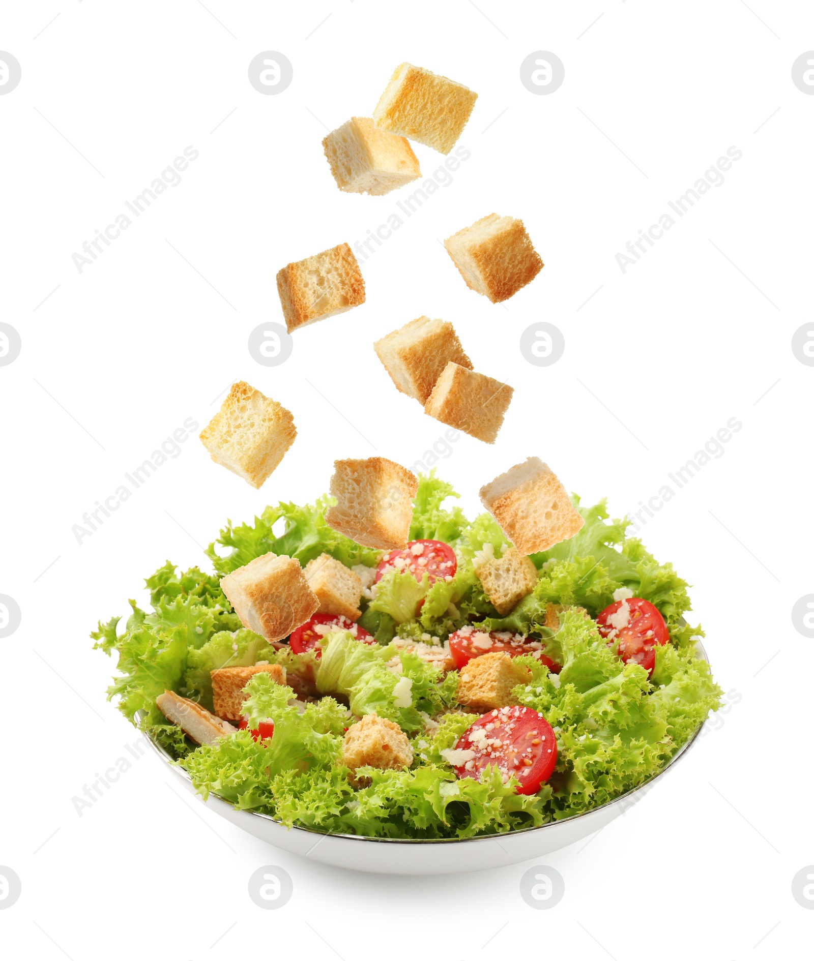 Image of Croutons falling into bowl of salad against white background