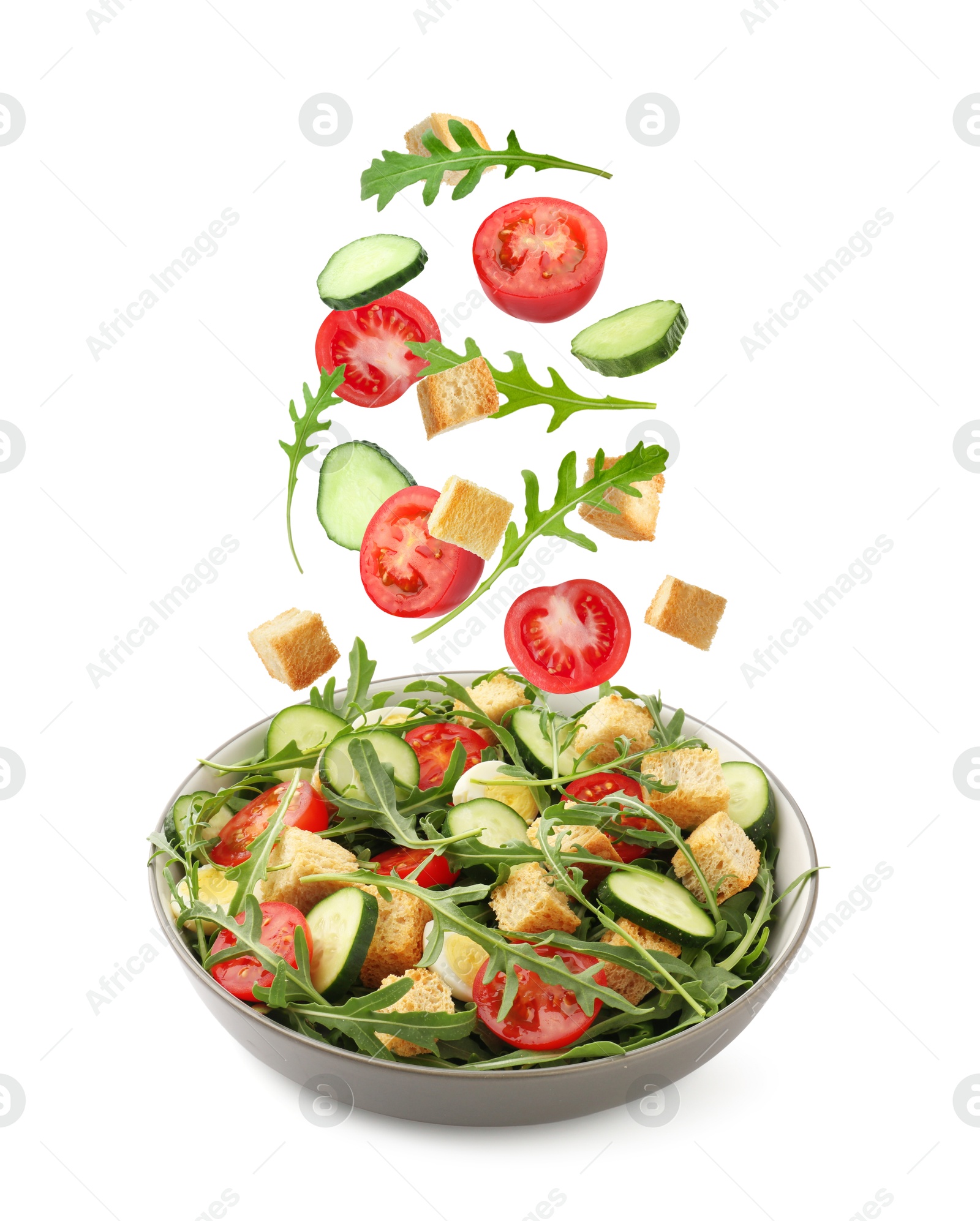 Croutons and other ingredients falling into bowl of salad against white background Image of Croutons and other ingredients falling into bowl of salad against white background