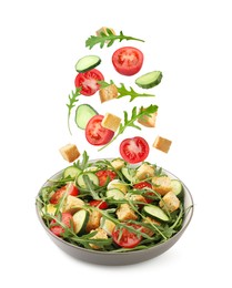 Image of Croutons and other ingredients falling into bowl of salad against white background