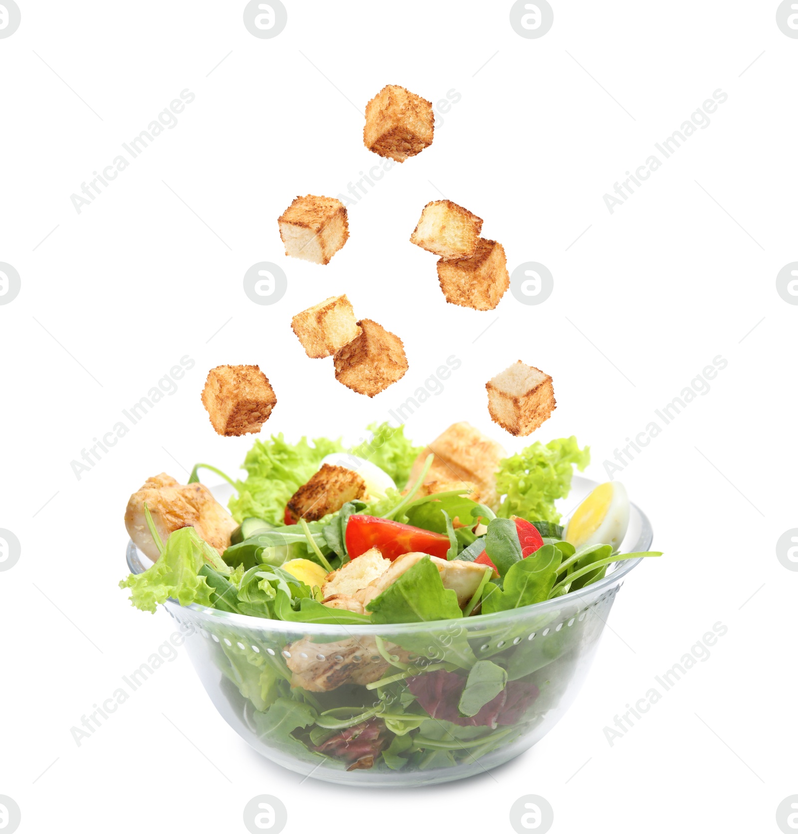 Image of Croutons falling into bowl of salad against white background