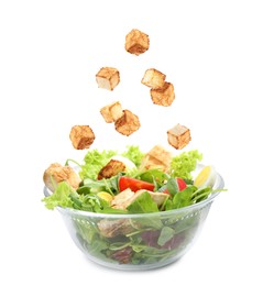 Image of Croutons falling into bowl of salad against white background