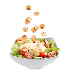 Image of Croutons falling into bowl of salad against white background