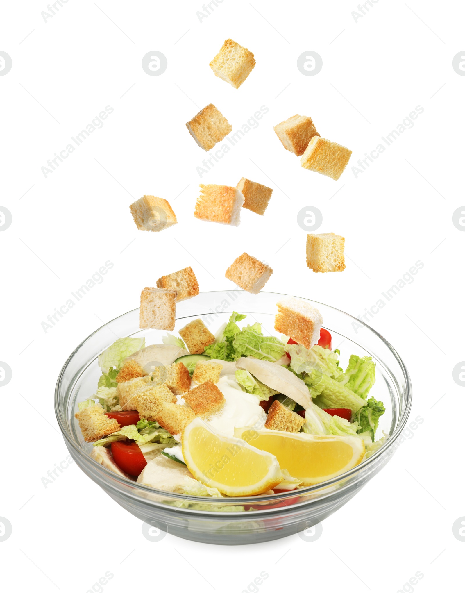 Image of Croutons falling into bowl of salad against white background