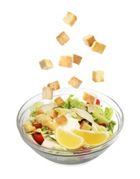 Image of Croutons falling into bowl of salad against white background