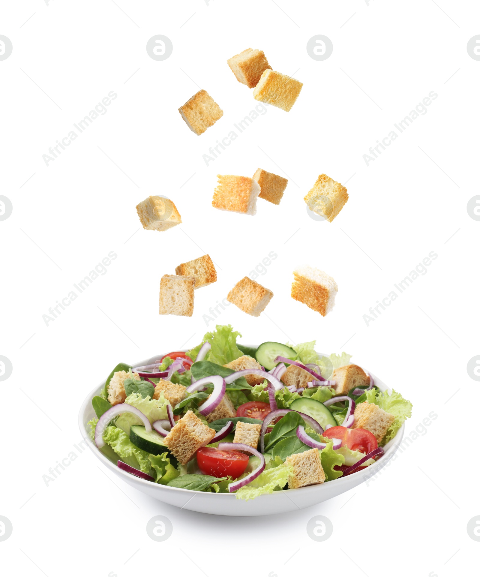 Image of Croutons falling into bowl of salad against white background