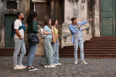 Photo of Guide with microphone and group of tourists on city street during excursion