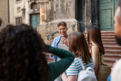 Photo of Guide with microphone and group of tourists on city street during excursion