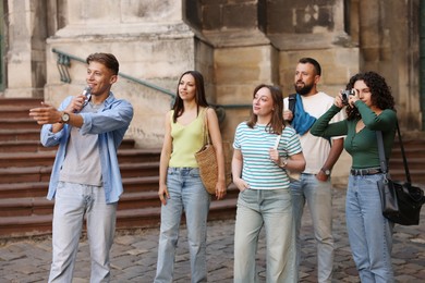 Photo of Guide with microphone and group of tourists on city street during excursion