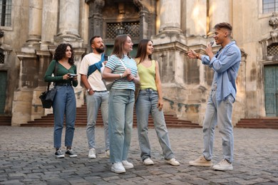 Photo of Guide with microphone and group of tourists on city street during excursion