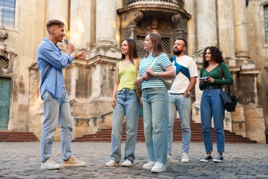 Photo of Guide with microphone and group of tourists on city street during excursion