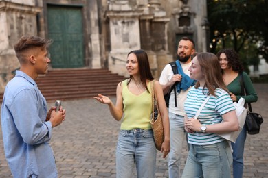 Photo of Guide with microphone and group of tourists on city street during excursion