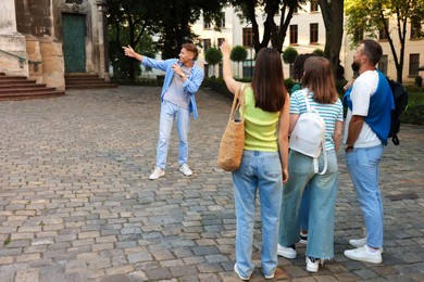 Photo of Guide with microphone and group of tourists on city street during excursion