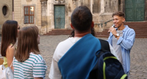 Photo of Guide with microphone and group of tourists on city street during excursion