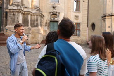 Photo of Guide with microphone and group of tourists on city street during excursion
