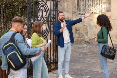 Photo of Guide with microphone and group of tourists on city street during excursion