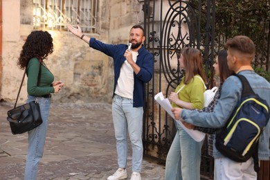 Photo of Guide with microphone and group of tourists on city street during excursion