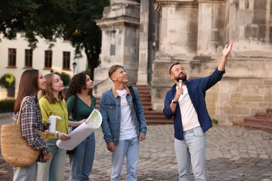 Photo of Guide with microphone and group of tourists on city street during excursion