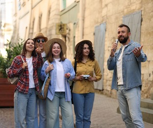 Photo of Guide with microphone and group of tourists on city street during excursion