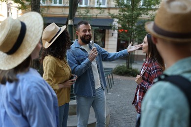 Photo of Guide with microphone and group of tourists on city street during excursion