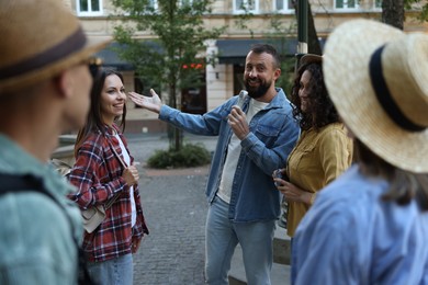 Photo of Guide with microphone and group of tourists on city street during excursion