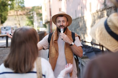 Photo of Guide with microphone and tourists on city street during excursion