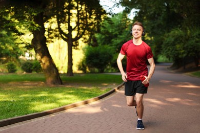 Photo of Smiling sportsman in headphones running with bottle outdoors. Morning exercise