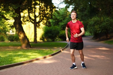 Photo of Smiling sportsman in headphones running with bottle outdoors. Morning exercise