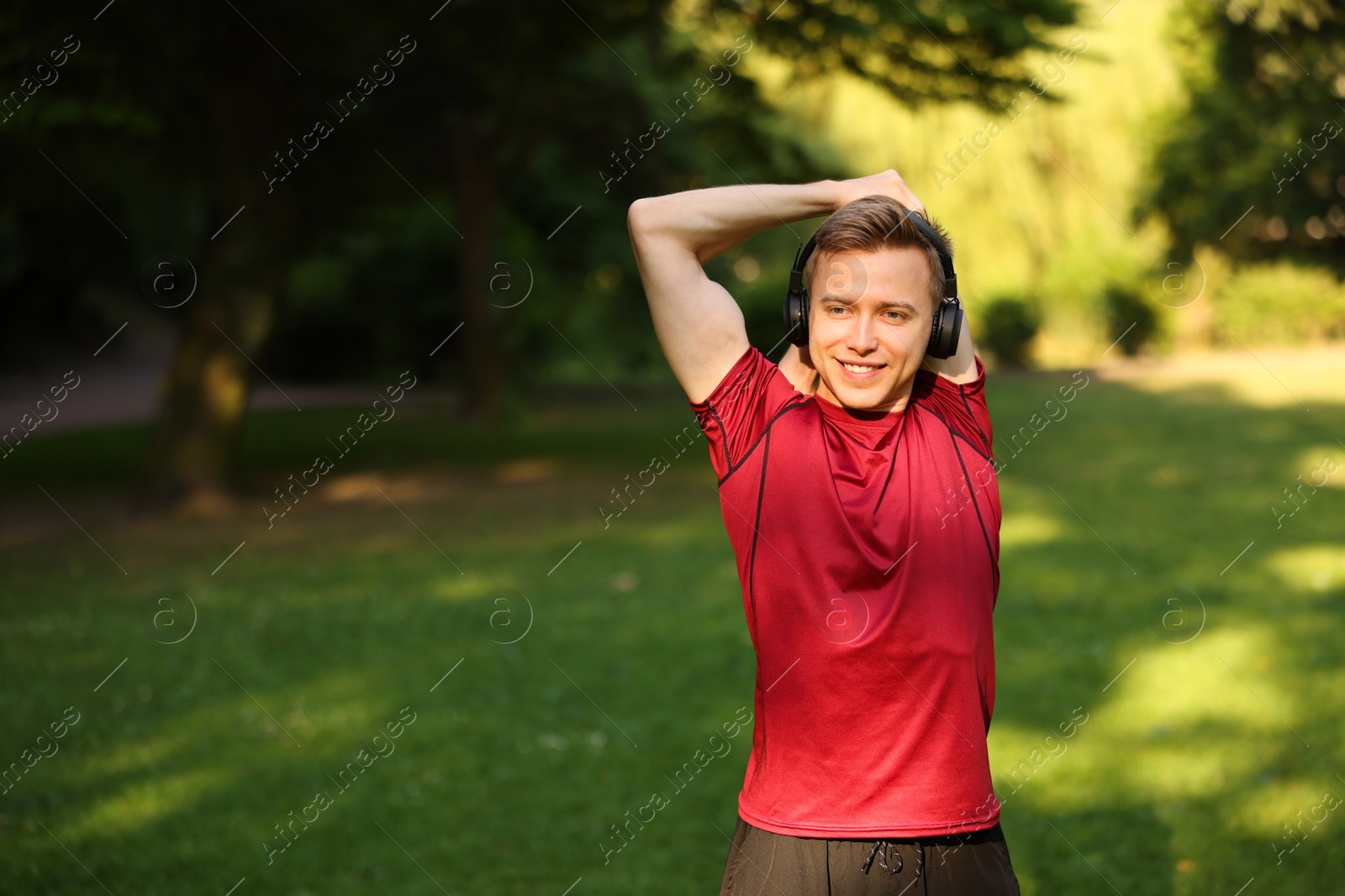 Photo of Smiling sportsman in headphones doing morning exercise outdoors. Space for text