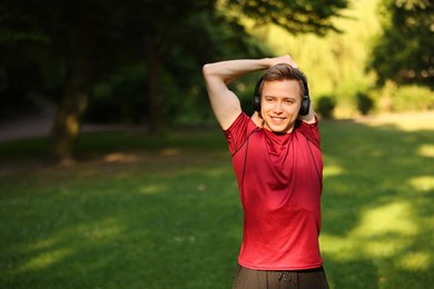Photo of Smiling sportsman in headphones doing morning exercise outdoors. Space for text