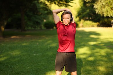 Photo of Smiling sportsman in headphones doing morning exercise outdoors. Space for text