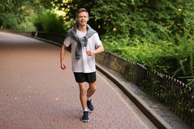Photo of Smiling sportsman in headphones running outdoors. Morning exercise