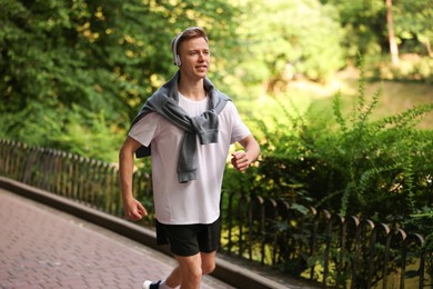 Photo of Smiling sportsman in headphones running outdoors. Morning exercise