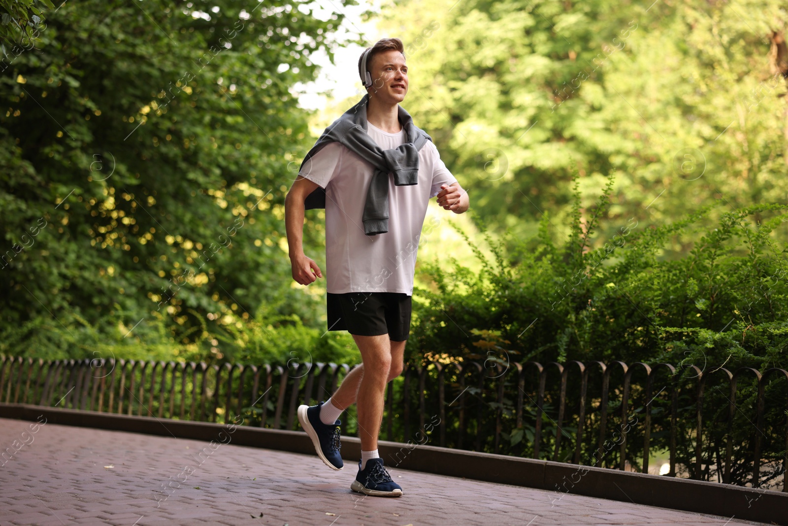 Photo of Smiling sportsman in headphones running outdoors. Morning exercise