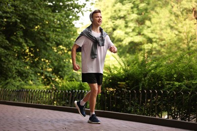 Photo of Smiling sportsman in headphones running outdoors. Morning exercise