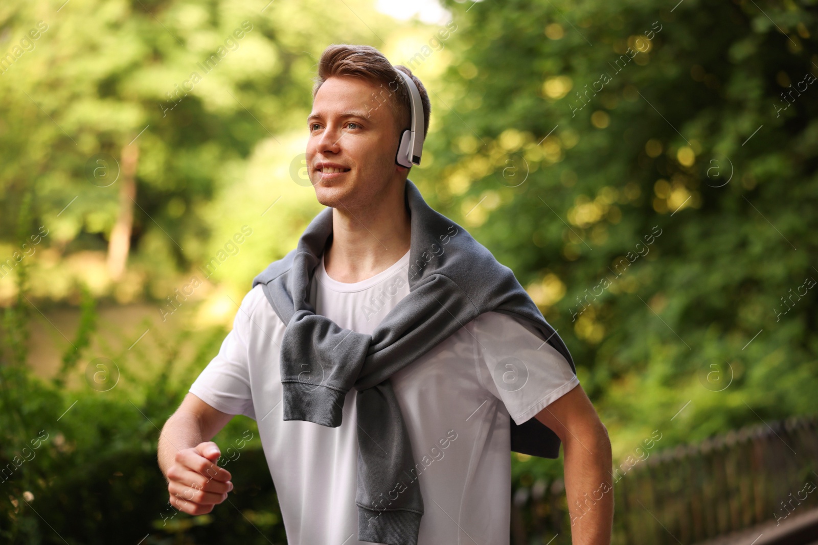 Photo of Smiling sportsman in headphones running outdoors. Morning exercise