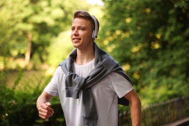 Photo of Smiling sportsman in headphones running outdoors. Morning exercise