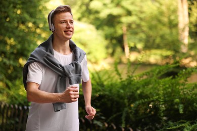 Photo of Smiling sportsman in headphones running outdoors, space for text. Morning exercise