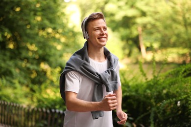 Photo of Smiling sportsman in headphones running outdoors. Morning exercise