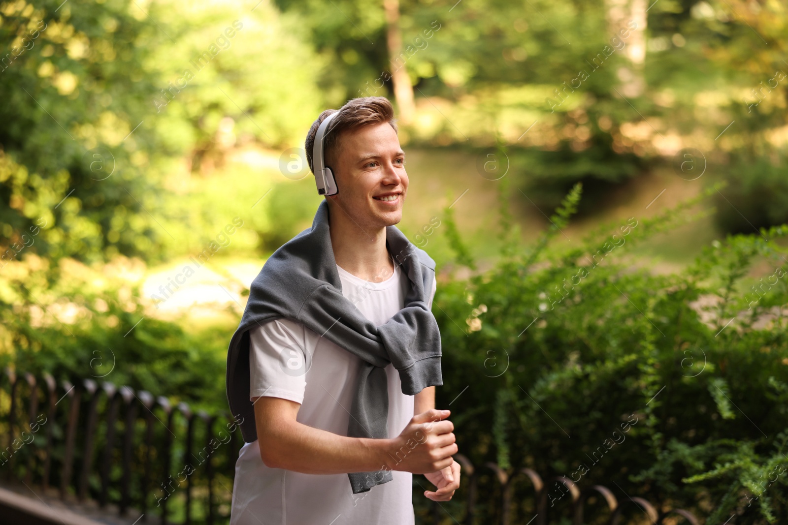 Photo of Smiling sportsman in headphones running outdoors. Morning exercise