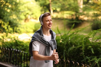 Photo of Smiling sportsman in headphones running outdoors. Morning exercise