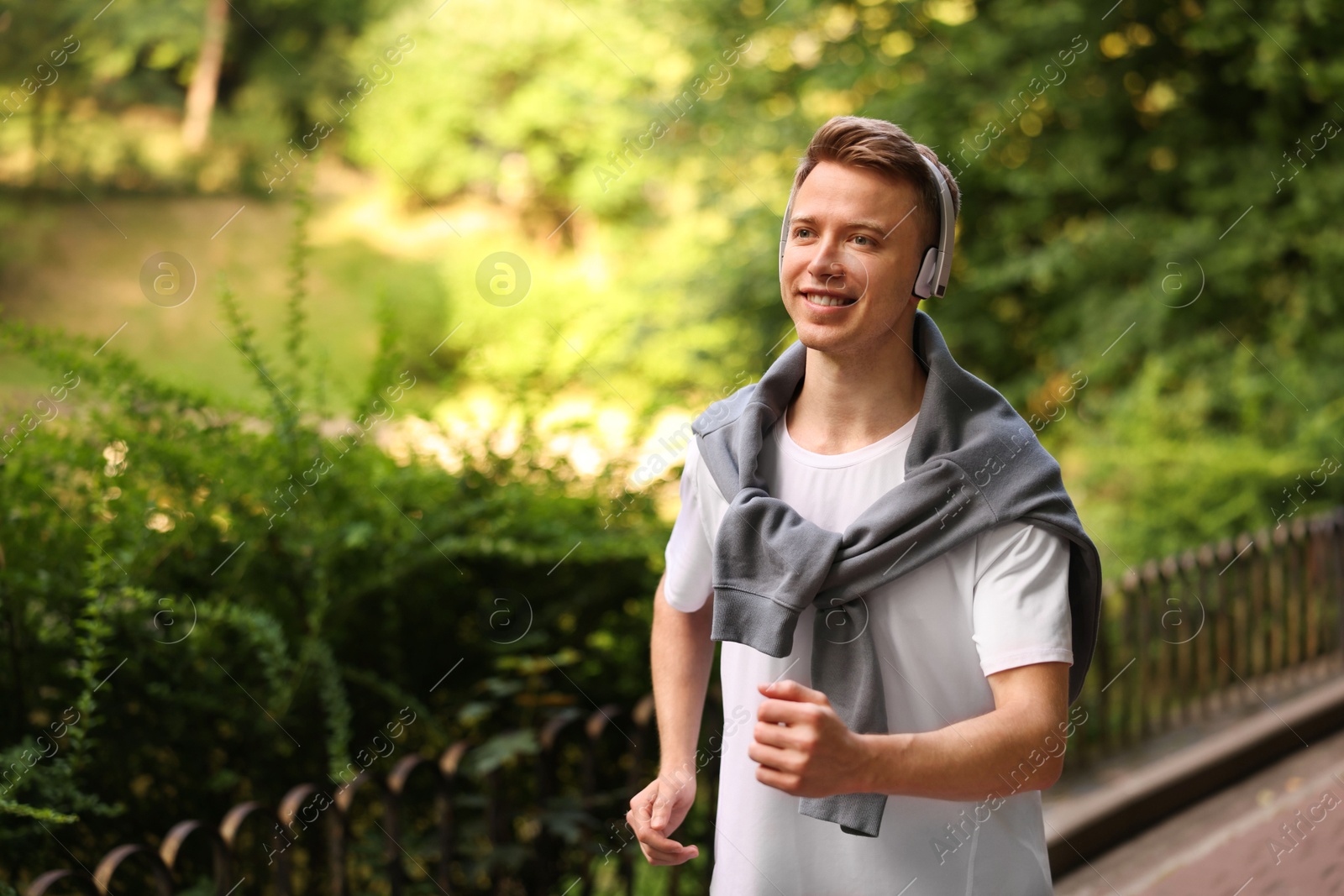 Photo of Smiling sportsman in headphones running outdoors, space for text. Morning exercise