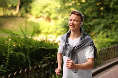 Photo of Smiling sportsman in headphones running outdoors, space for text. Morning exercise
