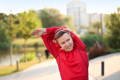 Photo of Smiling sportsman in headphones doing morning exercise outdoors. Healthy lifestyle