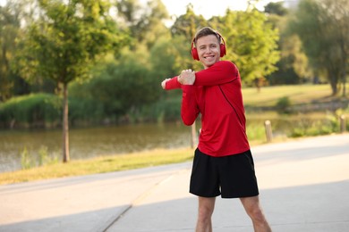 Photo of Smiling sportsman in headphones doing morning exercise outdoors. Space for text