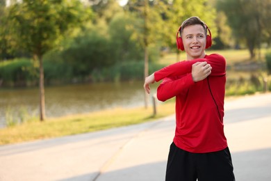 Photo of Smiling sportsman in headphones doing morning exercise outdoors. Space for text
